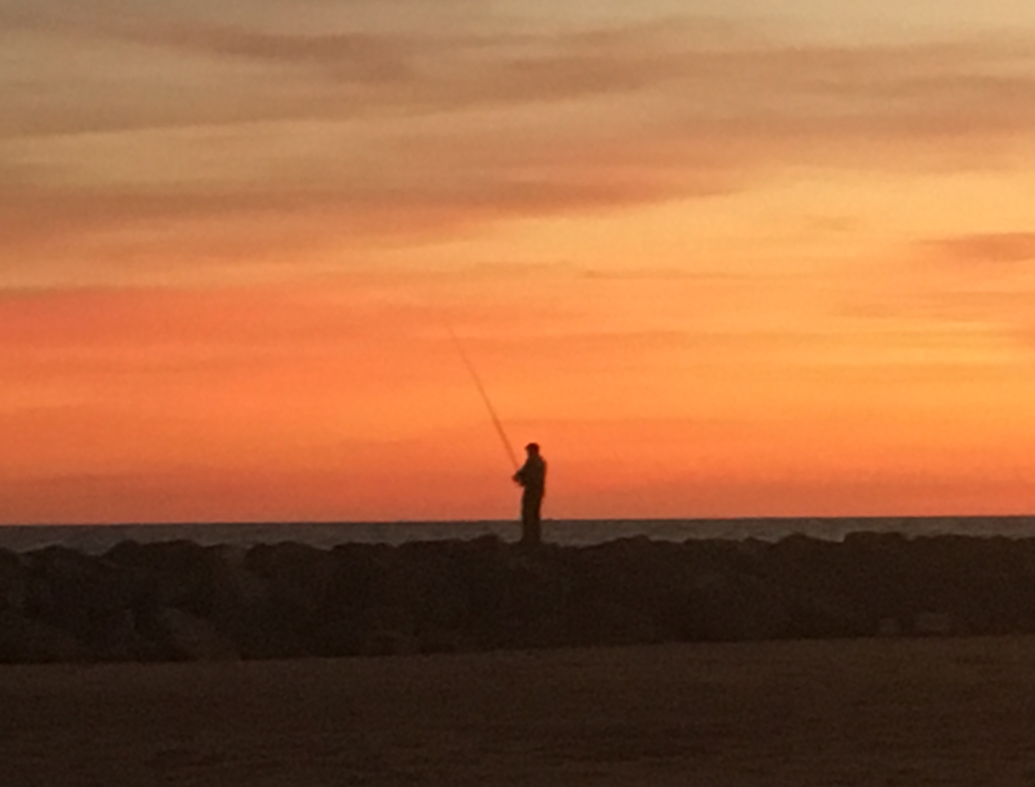 Silueta de pescador al atardecer sobre las rocas del mar